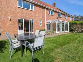 A garden with a glass table and six chairs outside a brick house with open doors at Cedar View in Hainford near Coltishall