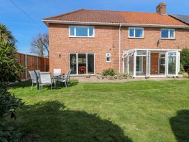 A backyard with green lawn and outdoor dining furniture beside a brick house with a glass conservatory at Cedar View in Hainford near Coltishall