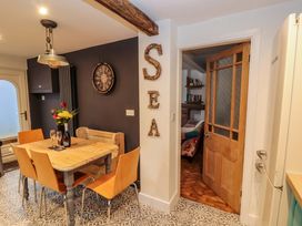 A dining area with a wooden table, four chairs, a wall clock, and a door leading to a room with a sofa at Seahaven in Allonby