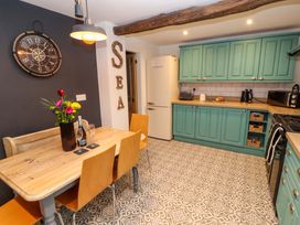 A kitchen with a wooden dining table and chairs a black wall clock and turquoise green cupboards at Seahaven in Allonby