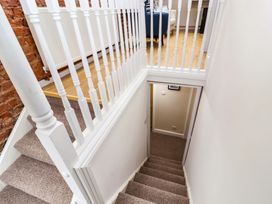 A carpeted staircase with white wooden balusters next to a brick wall leading down to a hallway with light walls at Seahaven in Allonby