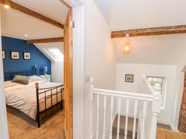 A bedroom with a bed and nightstand next to a hallway with white railing and wooden beams at Seahaven in Allonby