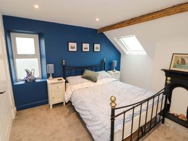 A bedroom with a black metal bed, bedside tables with lamps, a blue accent wall, and a small window at Seahaven in Allonby