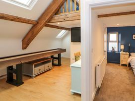 A room with exposed wooden beams a shuffleboard table and a cabinet next to a hallway leading to a bedroom with a blue accent wall and a bed at Seahaven in Allonby