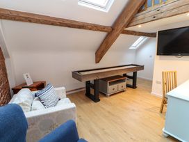 A room with a shuffleboard table a sofa with cushions a blue chair a wall-mounted TV and wooden beams at Seahaven in Allonby