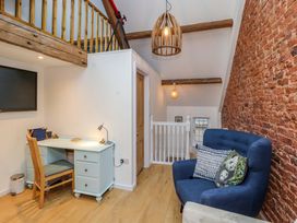 A small room with a blue armchair with cushions a white desk with a wooden chair a wall-mounted TV exposed wooden beams and a brick wall at Seahaven in Allonby