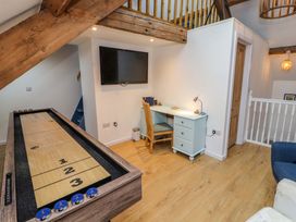 A game room with a shuffleboard table a wall-mounted television a desk with a chair and a wooden railing at Seahaven in Allonby