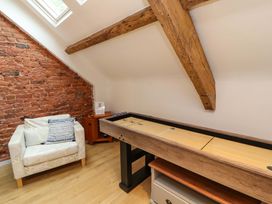 A room with a shuffleboard table a white armchair and a wooden side table under a skylight with exposed wooden beams at Seahaven in Allonby
