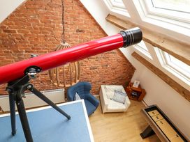 A room with a red telescope on a tripod a blue chair a white armchair a wooden side table and a game table under skylight windows at Seahaven in Allonby