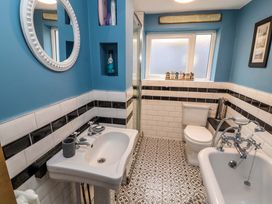 A bathroom with a sink toilet bathtub patterned floor and a round mirror on blue walls at Seahaven in Allonby