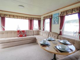 A beige sectional sofa with a red floral pillow and a round dining table set with plates bowls and cutlery at D12 Treetops in Clarach near Aberystwyth