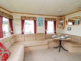 A corner seating area with a round dining table set with plates and bowls in a room with windows and burgundy curtains at D12 Treetops Clarach near Aberystwyth