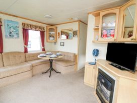 A living room with a corner sofa and round dining table set with plates a tv on a cabinet and a small fan at D12 Treetops in Clarach near Aberystwyth