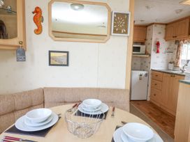 A dining area with a round table set with plates and bowls and a small kitchen with wooden cabinets and a refrigerator at D12 Treetops in Clarach near Aberystwyth