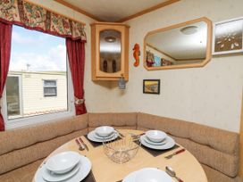 A dining area with a round table set with white dishes and brown cushioned seating at D12 Treetops Clarach near Aberystwyth