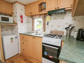 A kitchen with wooden cabinets a gas stove a microwave a small fridge a sink a kettle and utensils at D12 Treetops Clarach near Aberystwyth