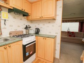 A kitchen with wooden cabinets a gas stove kettle toaster and utensils next to a living room with a sofa at D12 Treetops in Clarach near Aberystwyth