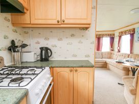 A kitchen area with a gas stove kettle and utensils next to a living area with a beige corner sofa and a dining table with plates at D12 Treetops in Clarach near Aberystwyth