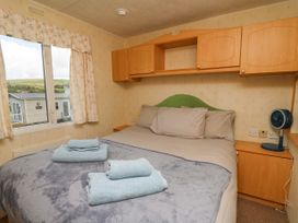 A bedroom with a bed, gray blankets, folded towels, wooden cabinets, a window with curtains, and a small fan on a wooden nightstand at D12 Treetops in Clarach near Aberystwyth