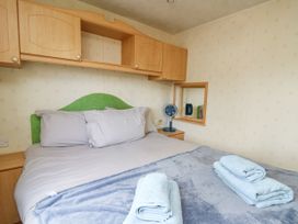A bedroom with a bed with pillows and folded towels and overhead wooden cabinets at D12 Treetops in Clarach near Aberystwyth