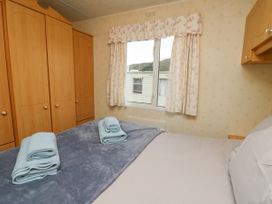 A bedroom with a bed covered in a gray blanket and folded towels on top next to wooden wardrobes and a window with floral curtains at D12 Treetops Clarach near Aberystwyth
