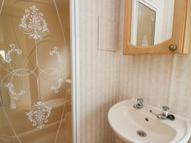 A bathroom with a sink and a mirror cabinet above it and a shower area with patterned glass at D12 Treetops Clarach near Aberystwyth