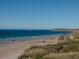 A beach with a distant lighthouse and rock formations at Chalet 3 Wipeout in Hayle