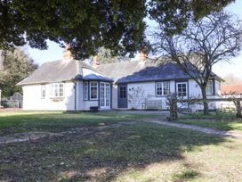 An exterior view of a single-story house with white wooden siding and multiple chimneys surrounded by grass and trees at Holm Oak Lodge in Tendring near Weeley