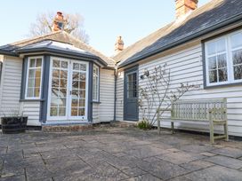 An outdoor patio area with stone paving a wooden bench potted plants white house walls and glass doors at Holm Oak Lodge in Tendring near Weeley