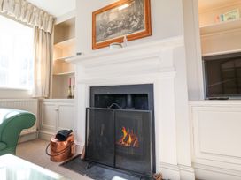 A living room with a lit fireplace a green chair built in cabinets and a television at Holm Oak Lodge in Tendring near Weeley