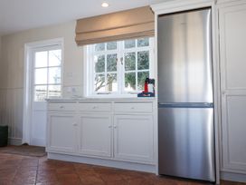 A kitchen with white cabinets a stainless steel refrigerator a window with a beige blind and a door at Holm Oak Lodge in Tendring near Weeley