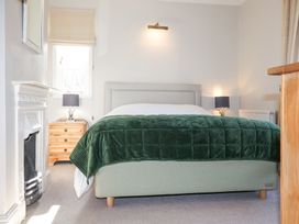 A bedroom with a bed covered by a green blanket two bedside tables with lamps a fireplace and a window at Holm Oak Lodge in Tendring near Weeley
