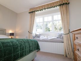 A bedroom with a green bedspread window seat with cushions and towels wooden dresser and beige curtains at Holm Oak Lodge in Tendring near Weeley