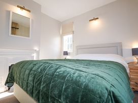 A bedroom with a bed covered with a green quilt a bedside table with a lamp and a mirror on the wall at Holm Oak Lodge in Tendring near Weeley