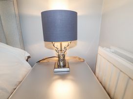 A bedside table with a lamp featuring a deer head base next to a bed and radiator at Holm Oak Lodge in Tendring near Weeley