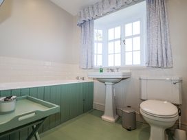 A bathroom with a bathtub a pedestal sink a toilet a small trash bin and a window with curtains at Holm Oak Lodge in Tendring near Weeley
