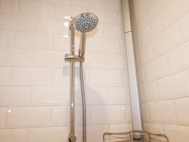 A showerhead with a sliding rail and a wire shelf in a tiled shower area at Holm Oak Lodge in Tendring near Weeley