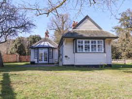 A house with white wooden siding and multiple windows surrounded by trees and grass at Holm Oak Lodge in Tendring near Weeley