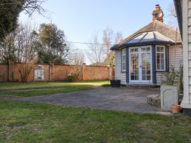 A garden with grass and a paved patio area with a house featuring large windows and a brick wall in the background at Holm Oak Lodge in Tendring near Weeley