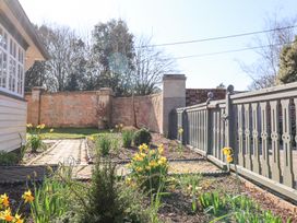 A garden with yellow flowers and a paved pathway next to a house and a wooden fence at Holm Oak Lodge in Tendring near Weeley