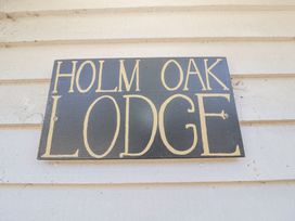 A wooden sign with the text Holm Oak Lodge on a light-colored wooden wall at Holm Oak Lodge in Tendring near Weeley