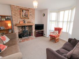 A living room with two sofas a red cushioned wooden chair a brick fireplace and a television near a window at Tulip Cottage in Staithes