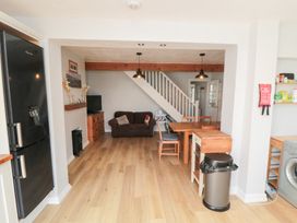 An open plan kitchen and living area with a black refrigerator dining table wooden chairs brown sofa and a washing machine at Tulip Cottage in Staithes