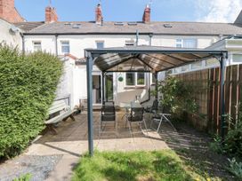 A backyard patio with glass table and chairs under a metal gazebo and a bench nearby at Tulip Cottage in Staithes
