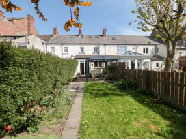 A backyard garden with a grass lawn a hedge wooden fence patio table and chairs and a row of terraced houses in the background