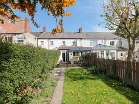A garden with grass, a paved path, a hedge on the left, a wooden fence on the right, and a patio with outdoor furniture at Tulip Cottage in Staithes