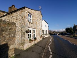 A stone house with flower baskets on the wall next to a road with a no left turn sign at Holme Fell View in Sedbergh