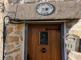 A wooden door with a small window and a black knocker next to a mailbox numbered 23 at Holme Fell View in Sedbergh