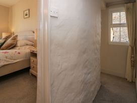 A bedroom with a bed and bedside table next to a hallway with a window and curtains at Holme Fell View in Sedbergh