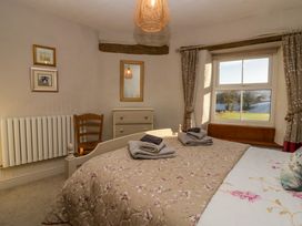 A bedroom with a bed and folded towels on it a wooden chair a chest of drawers a window with curtains and a view outside at Holme Fell View in Sedbergh